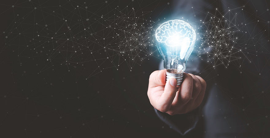 A hand holds a glowing light bulb.